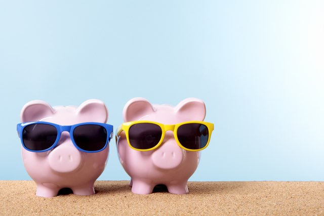 Two pink piggy banks on a beach with sunglasses.  Space for copy.  Studio shot with plain blue background - warm color and directional lighting are intentional.